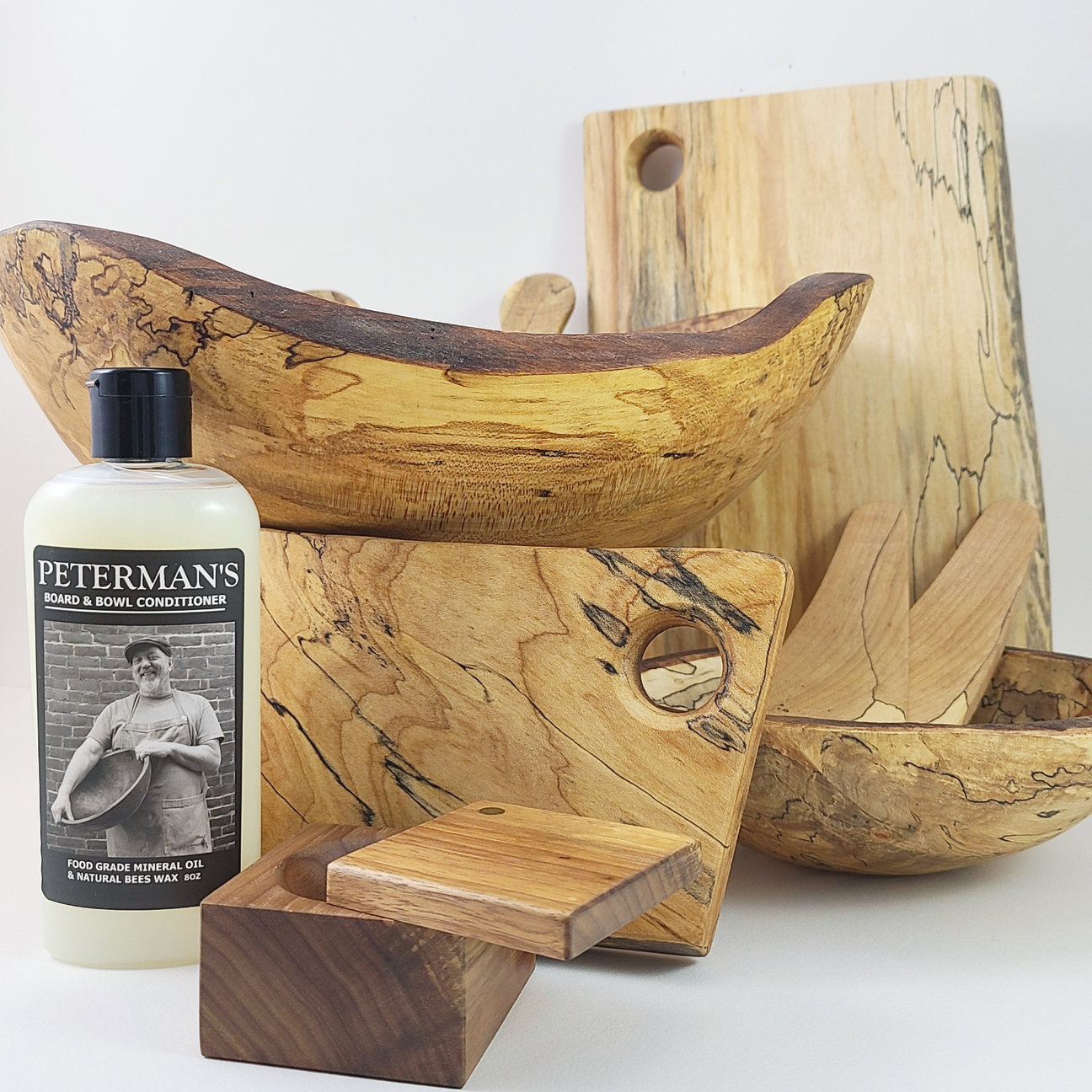 Wooden bowls and cutting boards with a bottle of board conditioner, featuring natural grain patterns.
