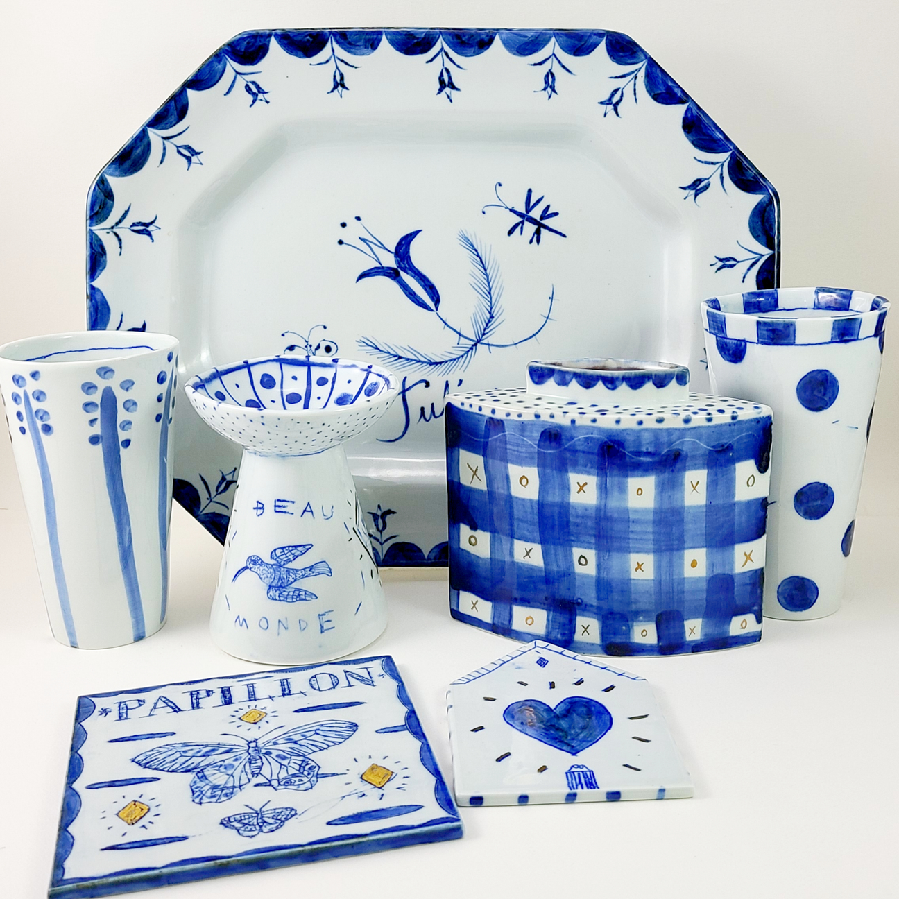 Blue and white ceramic set with floral, checkered, and polka dot patterns, featuring plates and vases.
