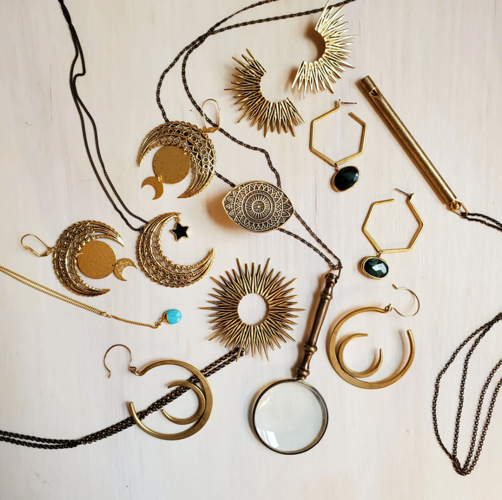 Gold jewelry with crescent moons, stars, and sunburst designs on a light wooden background.